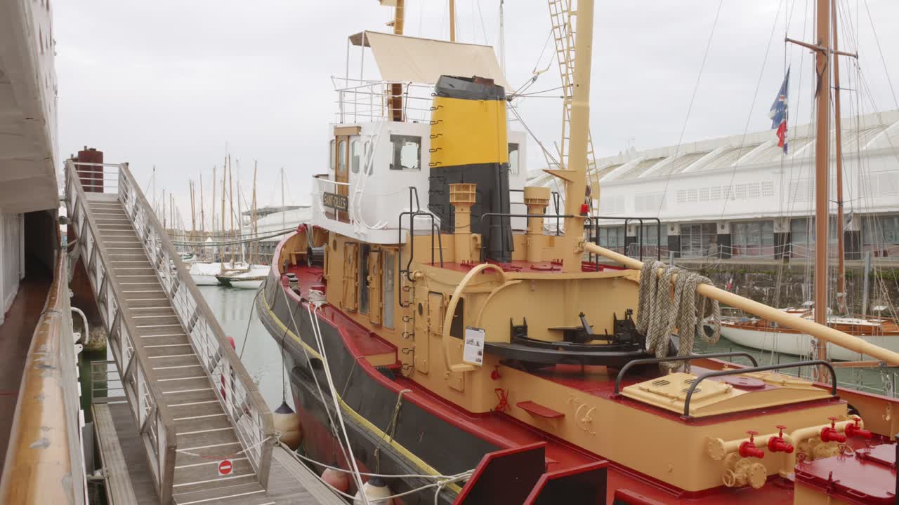 A historic tugboat docked in a harbor with other boats on an overcast day