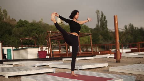 Mujer-Practicando-Yoga-En-La-Alfombra-En-La-Playa-Realizando-Asanas-De-Yoga-O-Estirando-Las-Piernas,-Inclinando-El-Torso-Hacia-Adelante-Con-La-Pierna-Levantada