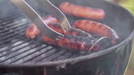 slow motion of tongs picking up gristly sausages from a smokey bbq grill