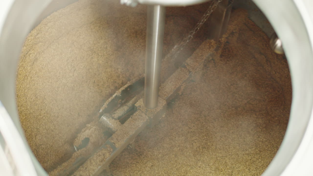 Craft beer production factory, brewery manufacture. Putting barley malt grains in conveyor close-up. Brewing, cooking alcohol in metal vats bottles