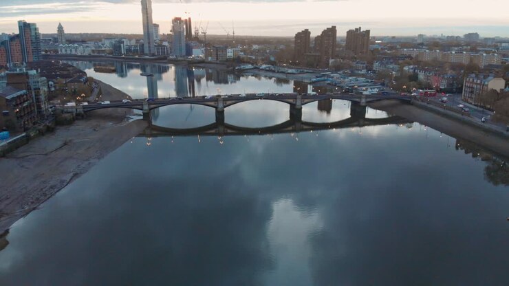 Ripresa da drone con movimento a gru discendente del traffico sul fiume Tamigi, Ponte di Battersea e porto di Chelsea a Londra al tramonto