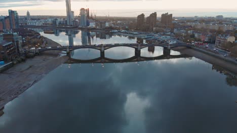 Falling-crane-drone-shot-of-thames-river-traffic-Battersea-bridge-and-Chelsea-harbour-London-at-sunset