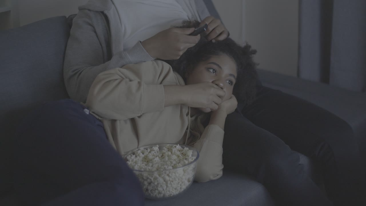 Young african american woman watching a movie and eating popcorn leaning on her boyfriend's lap