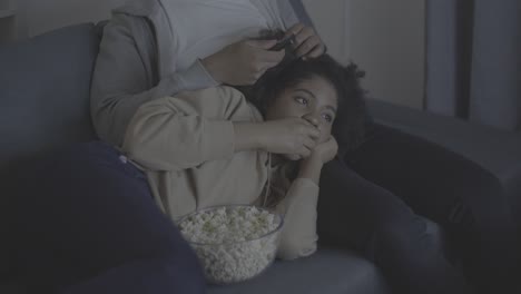 joven afroamericana viendo una película y comiendo palomitas de maíz apoyada en el regazo de su novio