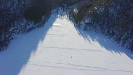 aerial top down view single person ice skating on frozen lake - wide snowy landscape