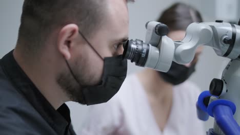 male dentist working with dental microscope in modern stomatology clinic. doctor using microscope for root canal treatment. stomatologist performs a surgical operation. cosmetic dentistry and surgery.