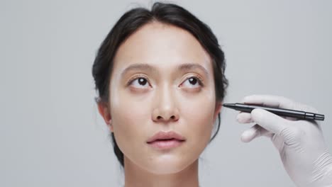 hand in glove examining face of asian woman on grey background, slow motion