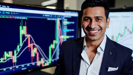 financial professional standing near digital monitors, showcasing candlestick charts displaying positive trading performance with confident, engaging smile