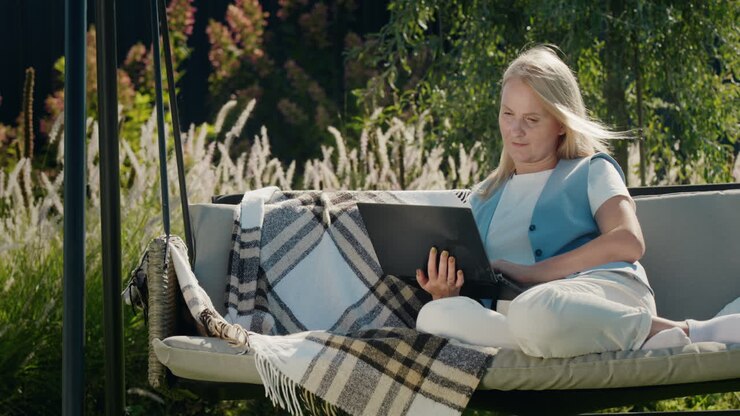 A young woman uses a laptop. Resting in a garden swing in the backyard of a house