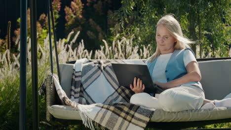 a young woman uses a laptop. resting in a garden swing in the backyard of a house