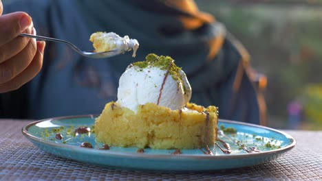 primer plano de una mujer comiendo un delicioso postre con helado, pistachos y salsa de chocolate
