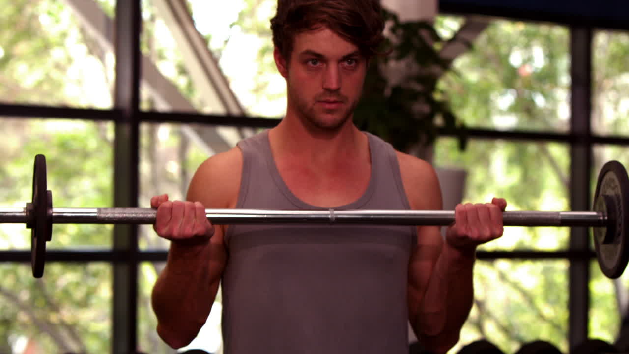 집중된 근육이 있는 남자가 덤벨을 들어 올리고 있습니다.