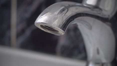 el agua está goteando del grifo de cromo roto gota por gota. la vista de cerca del agua goteando de un grifo brillante, grifo. se necesita un fontanero, fondo de bucle