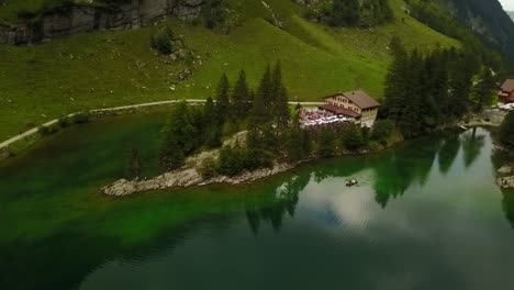 look from above on a calm green lake with boat and a hotel in between the trees