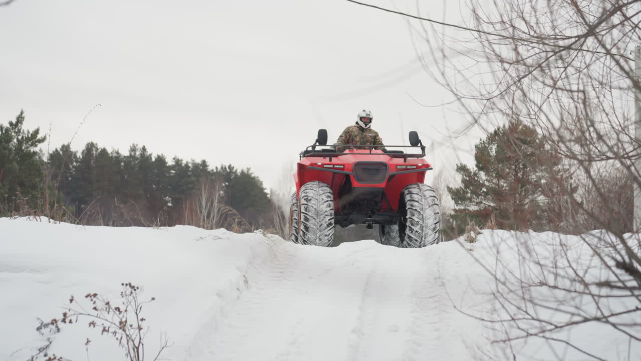 ATV rosso che scala una ripida collina innevata, una guida con casco affronta la salita lungo un sentiero dissestato in una foresta gelida, pneumatici robusti che fanno presa sul terreno ghiacciato sotto un cielo coperto, con un'atmosfera di spedizione avventurosa e all'aria aperta.