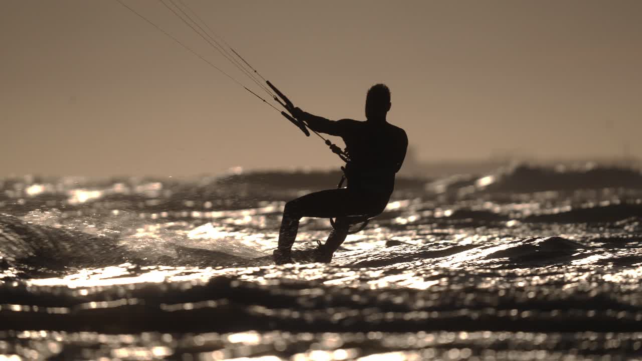 silueta de cámara lenta de kitesurfer saliendo al mar sobre pequeñas olas al atardecer