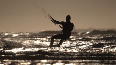 slow motion silhouette of kitesurfer going out to sea over small waves at sunset