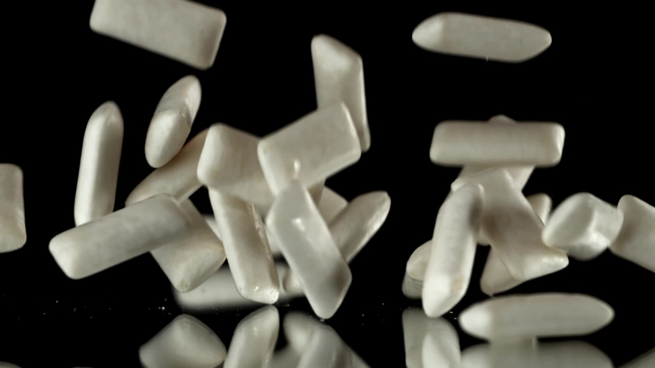 Pezzi di gomma da masticare bianchi che cadono al rallentatore su una superficie nera riflettente