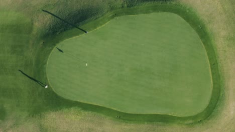 birdseye stationary drone shot of a golfer putting on a green with long shadows