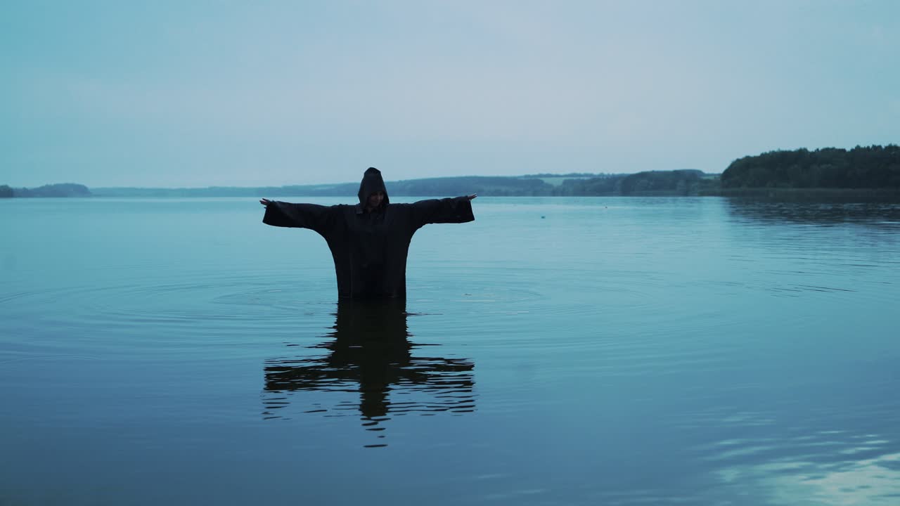 Female figure in black mantle in the river. Divination by the water