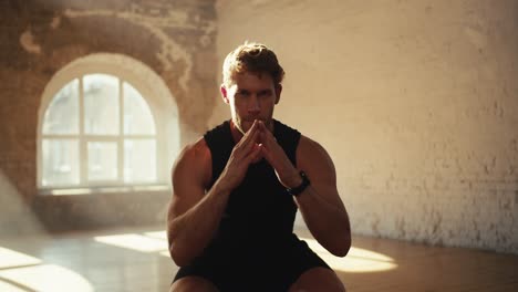 Close-up-shot-of-a-man-in-a-black-T-shirt-crouching-in-a-sunny-hall.-Sports-activities-in-a-special-brick-building