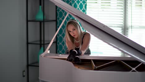 woman wearing a black dress leans over piano to pose in a seductive manner