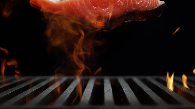 Salmon Fillet Falling Onto Charcoal Grill in Slow Motion, Fire Burst From Beneath The Grate on the Black Background