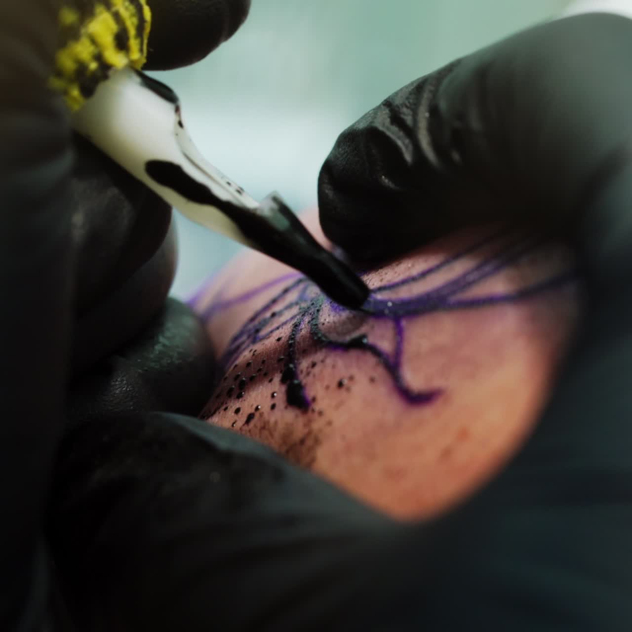 Covering the sketched picture with black ink. Tattooist wearing black gloves uses special ink machine at work. Close up