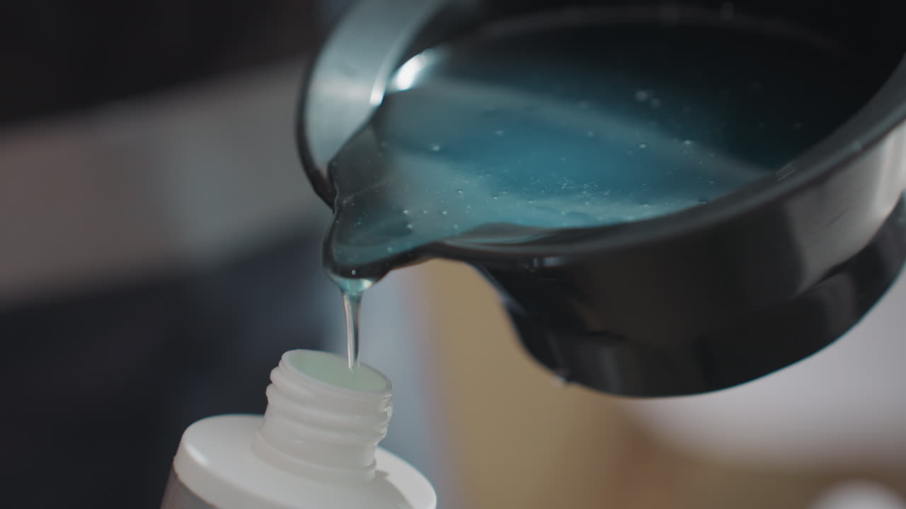 pigmento brillante vertiéndose de un cuenco en una botella, fluido azul iridiscente, bordes de alto contraste, puntería precisa y agarre firme, mostrador de salón tipo laboratorio, brillo del producto visible bajo la luz