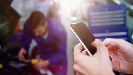 manos de una mujer usando un teléfono móvil mientras el mecánico muestra los pulgares hacia arriba