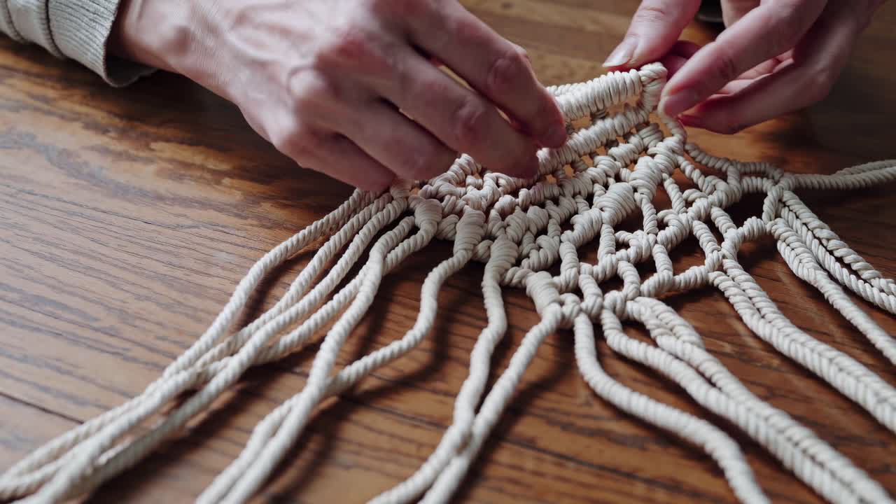 Close-up video of hands crafting macramé on a wooden table