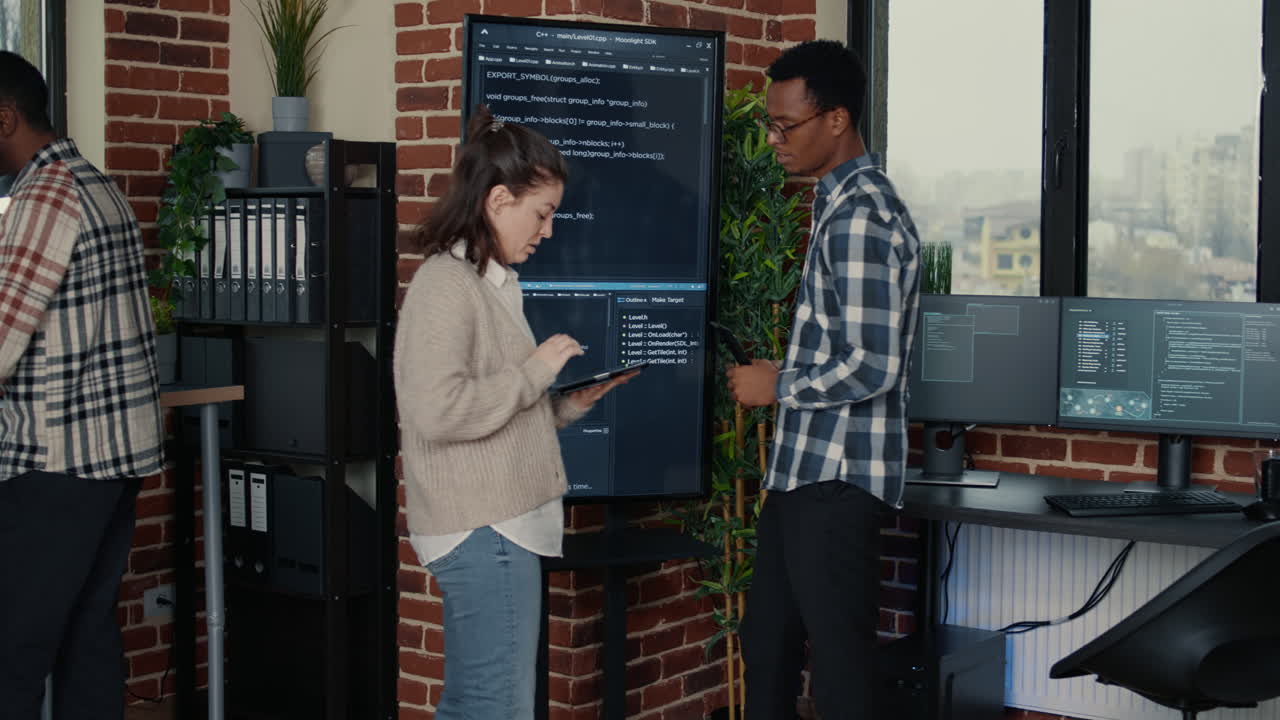Team of database admins analyzing source code on wall screen tv comparing errors using digital tablet