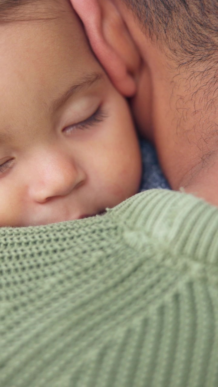 Primo piano di un neonato addormentato sulla spalla del padre