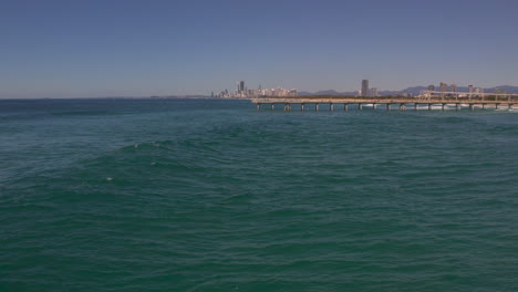 Aerial-view-of-drone-tracking-a-wave-as-it-forms-and-breaks-on-a-beautiful-day-with-the-popular-city-of-Surface-Paradise-in-the-background-at-The-Spit-Gold-Coast-QLD-Australia