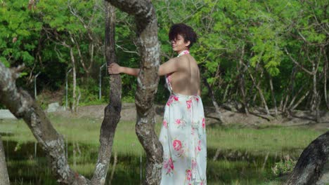 a hispanic woman walking between tree branches at the park in a long flowing flower dress