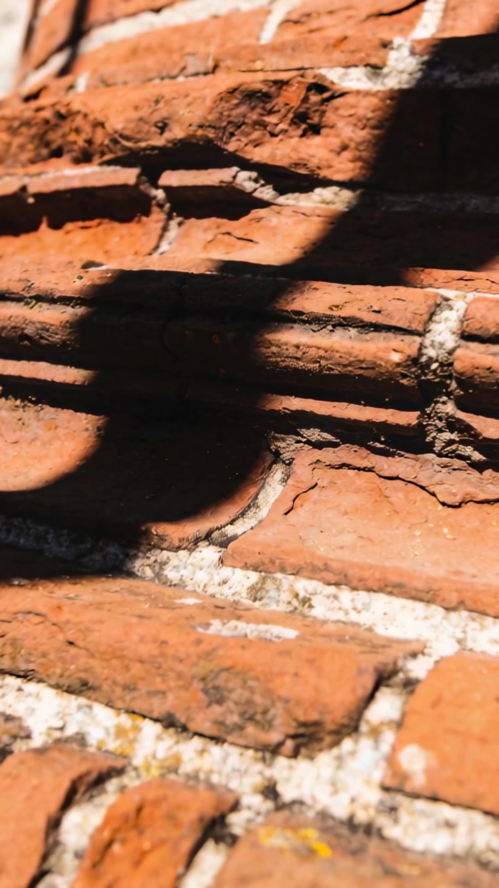 Vertical video: Panning camera following terracotta bricks in sun, revealing shadow, cracks, flecks