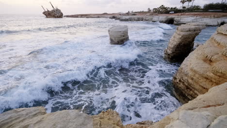 a powerful scene of waves crashing near a shipwreck on the rocky coast of cyprus, showcasing the dramatic landscape and maritime history