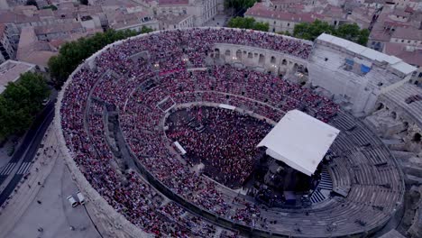 Tiro-Superior-De-Rotación-De-Drones-Sobre-La-Arena-De-Nimes-Al-Atardecer,-La-Gente-Está-Esperando-El-Concierto-De-Stromae