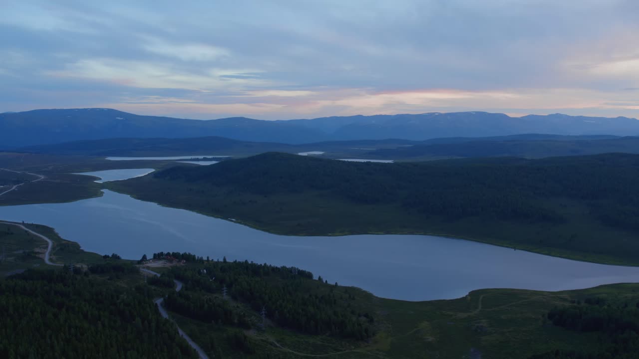 Il filmato del drone mostra un ampio fiume serpeggiante tra colline e montagne boscose all'ora blu, un tranquillo paesaggio estivo nella Repubblica dell'Altai, Siberia, Russia.