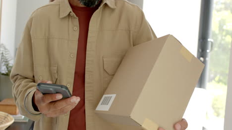 Holding smartphone, man carrying cardboard box and checking delivery details