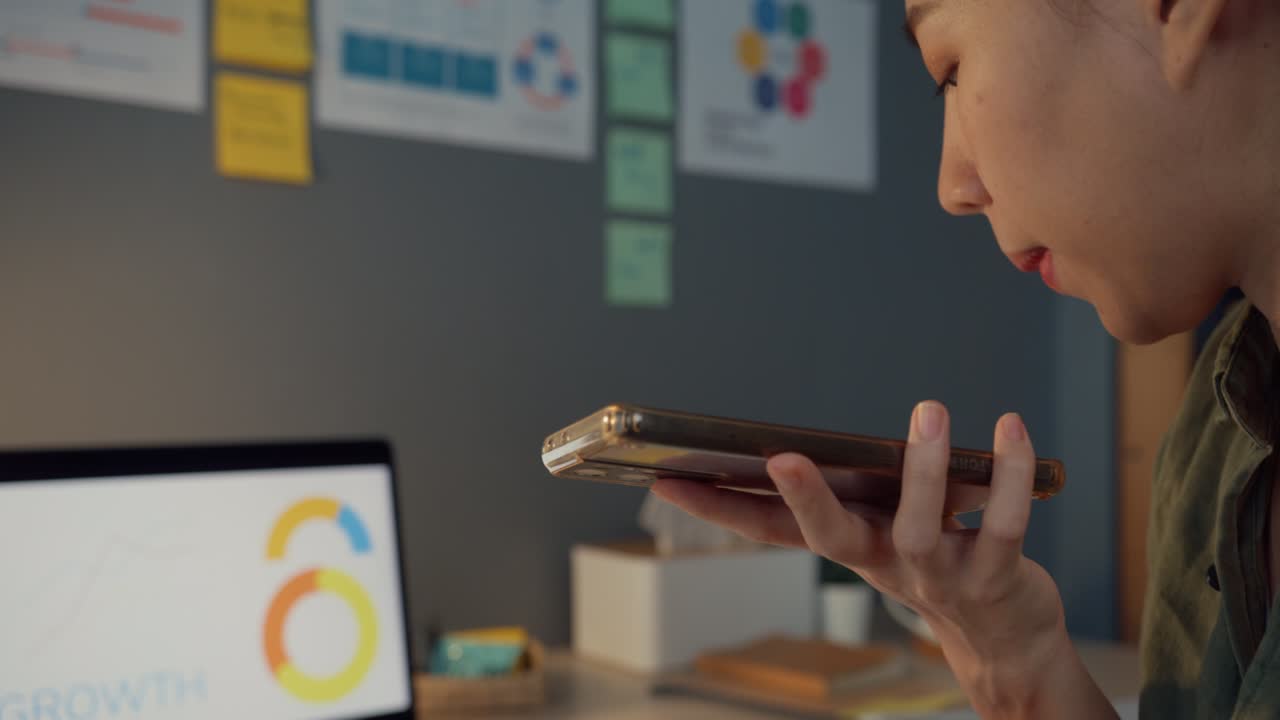 Young Asia business lady freelance using smart phone voice assistant app or loudspeaker talking with friends at office night.