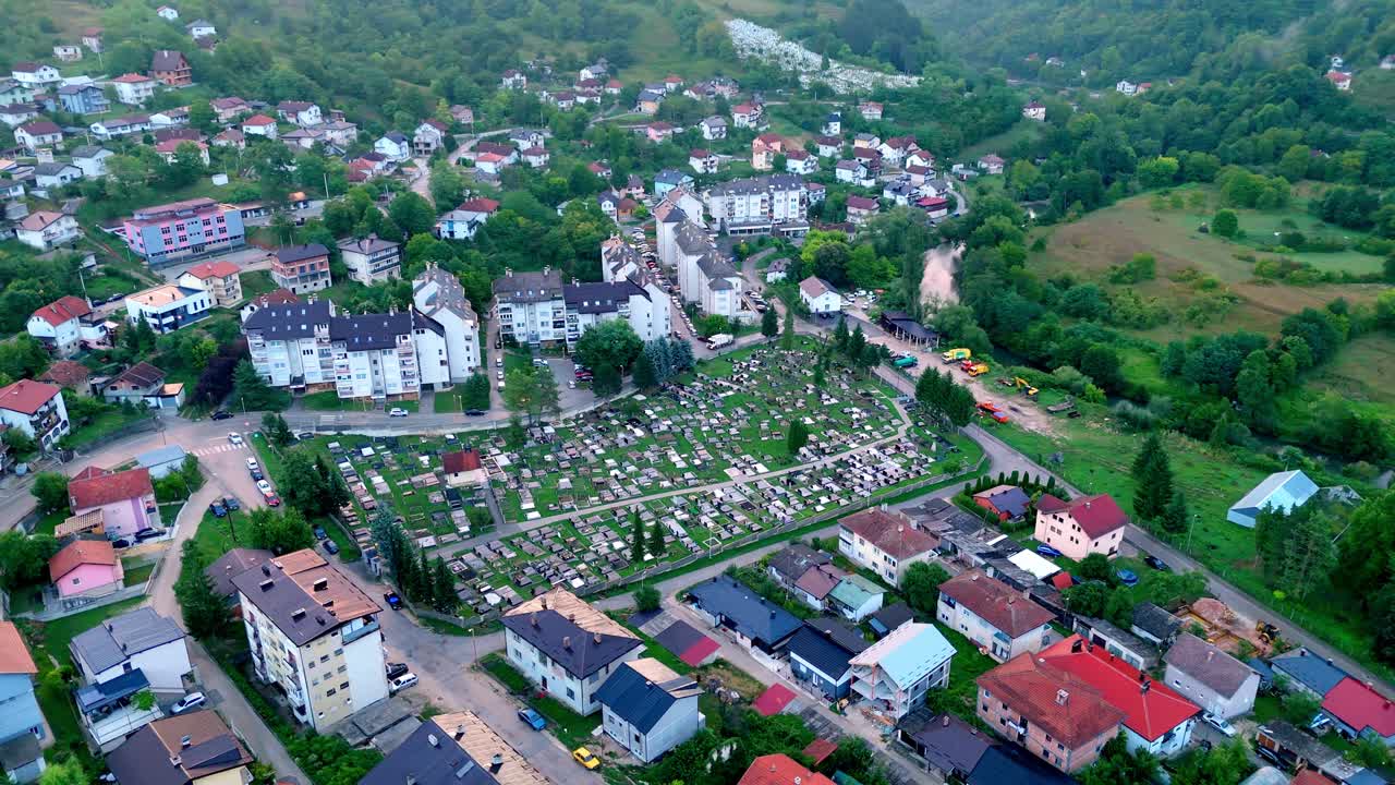 Aerial drone view of Jajce cemetery in Bosnia and Herzegovina, surrounded by historic town architecture and lush green hills under dramatic skies