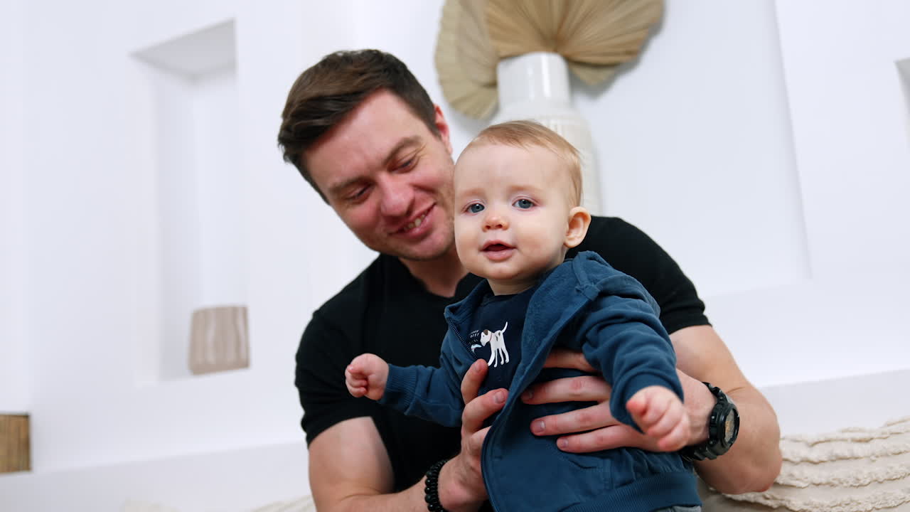 Man supports a cute little baby in blue sweatshirt. Adorable infant learning to stand. Dad and son concept.