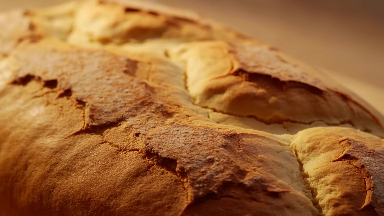 Primo piano dal basso di pane artigianale con crosta dorata e screpolata, mollica tenera a vista, consistenza rustica fatta a mano, illuminazione calda da panificio e sfondo sfocato e morbido per la presentazione del cibo.