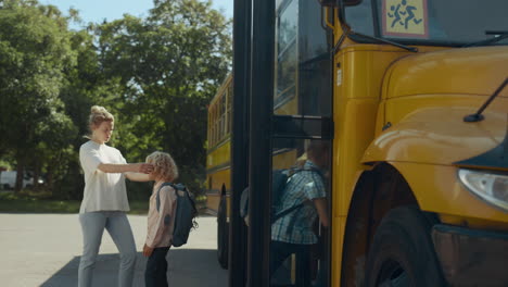 mother saying goodbye little son standing at bus. pupils boarding schoolbus.