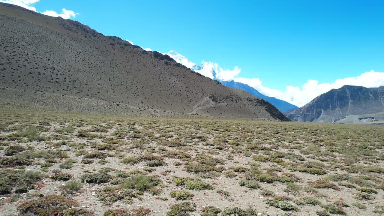 vastos y áridos campos con arbustos del desierto cerca de grandes y escarpadas montañas escarpadas cerca de kagbeni en la región de mustang de nepal - paso aéreo de baja altitud