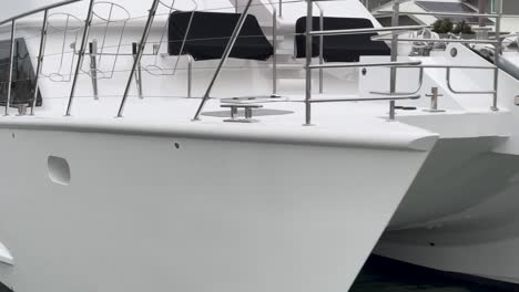 sailing past bow of a catamaran parked on a pontoon in a waterfront suburb