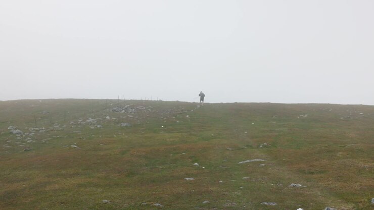 Static shot of a hiker walking along Ben Chonzie under heavy fog