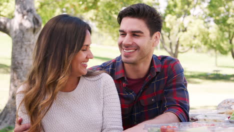 Joven-Pareja-Sonriente-Abrazándose-En-Una-Mesa-En-Un-Parque