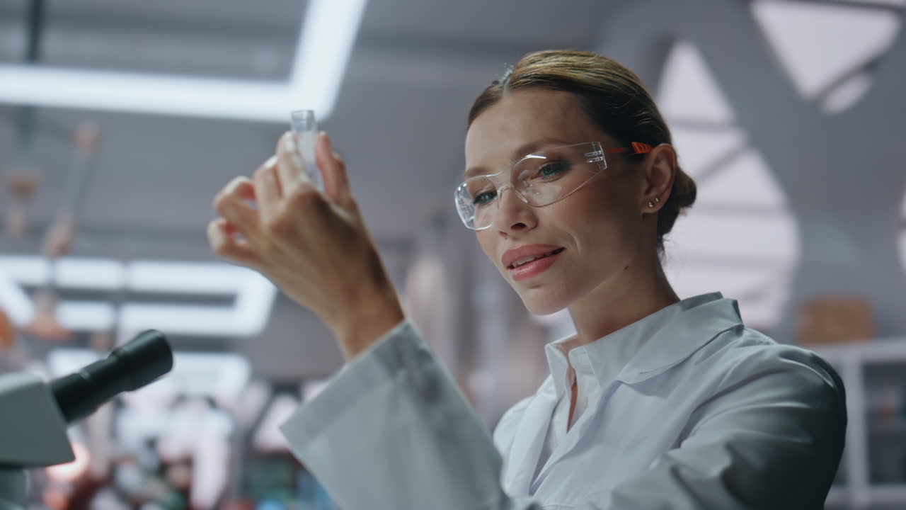 Smiling microbiologist examining test tube with medicines in laboratory closeup.